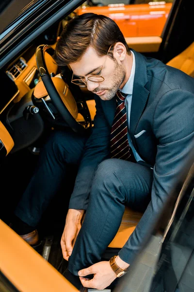 Vue grand angle de l'homme d'affaires dans les lunettes de réglage pantalon dans la voiture de luxe — Photo de stock