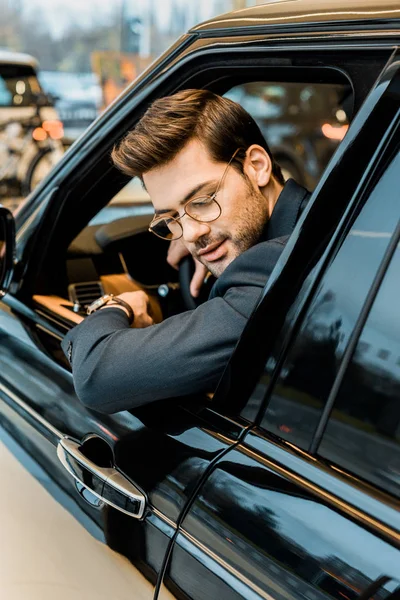 Selective focus of stylish businessman in eyeglasses looking out from window of automobile — Stock Photo