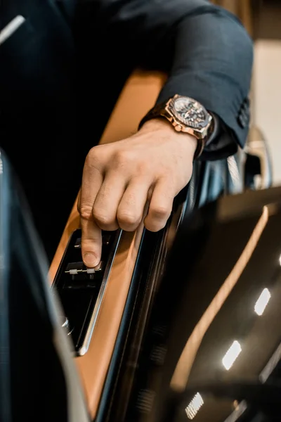 Cropped image of businessman with luxury watch pushing button for closing window of automobile — Stock Photo