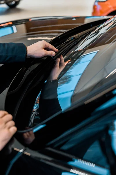 Cropped image of businessman adjusting windshield wipers of black automobile — Stock Photo