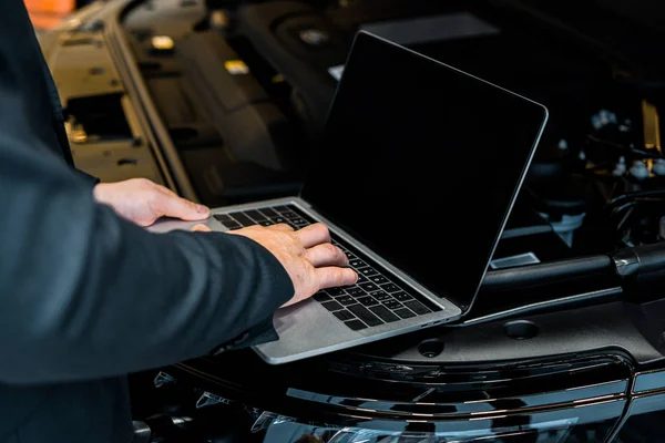 Visão parcial do empresário verificando o capô do carro com laptop com tela em branco — Fotografia de Stock