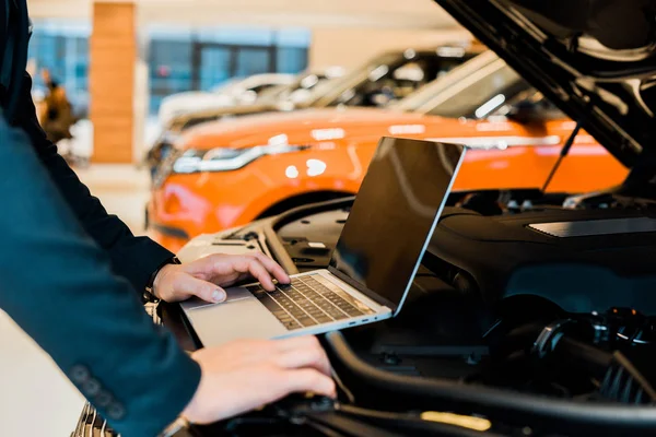 Обрезанное изображение бизнесмена, проверяющего капот автомобиля с ноутбуком с чистым экраном — стоковое фото