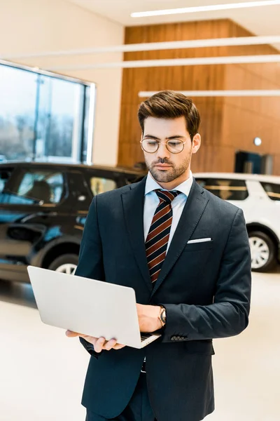 Selective focus of businessman in formal suit using laptop at dealership salon — Stock Photo