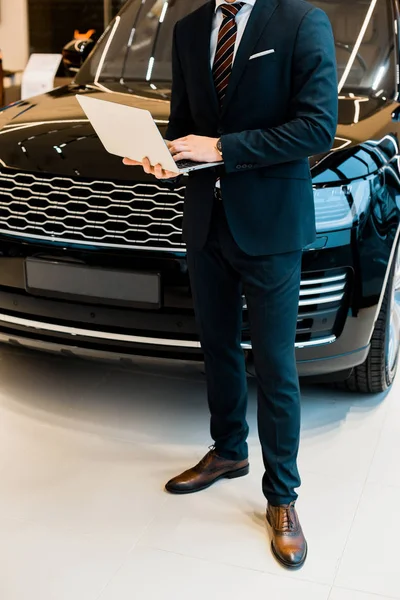 Partial view of businessman in formal suit using laptop at dealership salon — Stock Photo