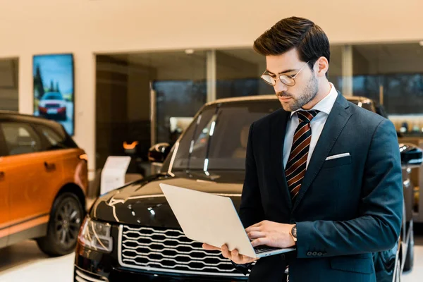 Handsome businessman in formal suit using laptop at dealership salon — Stock Photo