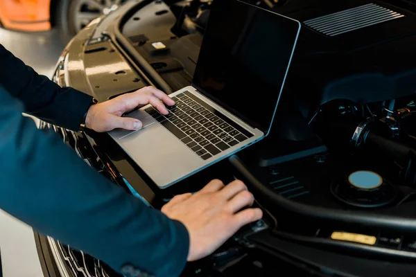 Vista parcial del empresario que comprueba la capucha del coche con el ordenador portátil con pantalla en blanco - foto de stock
