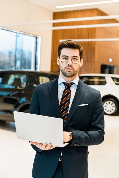 Stylish businessman in eyeglasses using laptop at dealership salon — Stock Photo