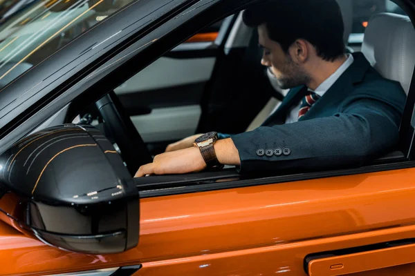 Enfoque selectivo de hombre de negocios elegante sentado en el coche naranja de lujo - foto de stock