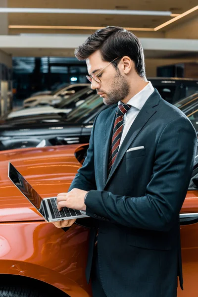 Seitenansicht des Geschäftsmannes in Brille mit Laptop in der Nähe von Automobil — Stockfoto