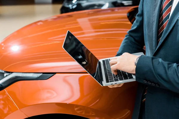 Imagem cortada de homem de negócios em óculos usando laptop perto de automóvel — Fotografia de Stock