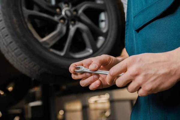 Imagem cortada do mecânico de automóveis masculino no trabalho geral segurando chave na oficina de reparação — Fotografia de Stock