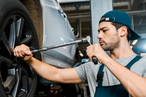 Focused male auto mechanic in working overall working with wheel wrench at auto mechanic shop — Stock Photo