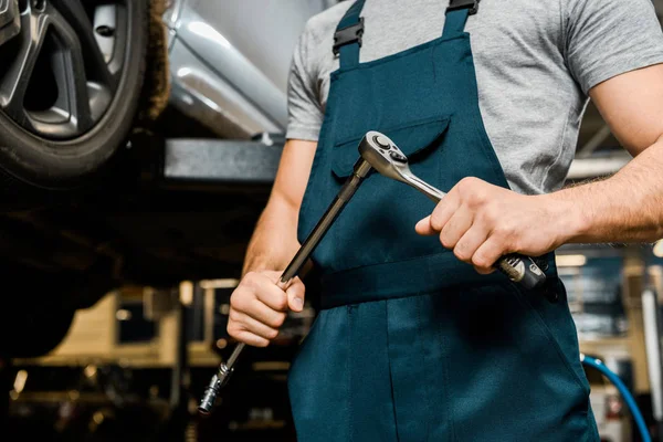 Cropped shot of auto mechanic with lug wrench in hands at mechanic shop — Stock Photo