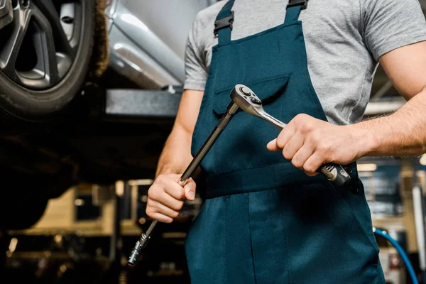 Tiro recortado de mecánico de automóviles con llave en las manos en el taller mecánico - foto de stock