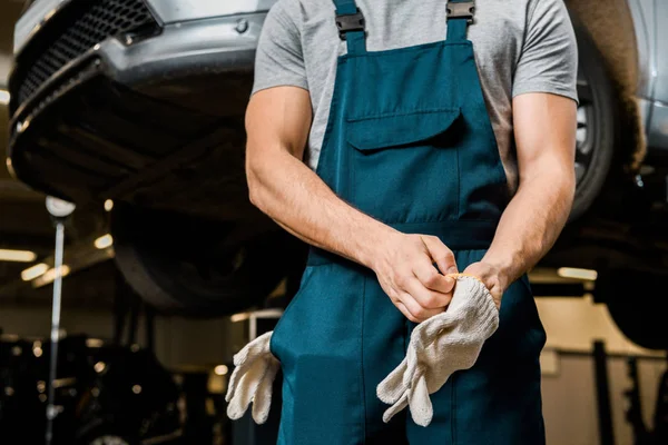 Partial view of auto mechanic in uniform wearing protective gloves at auto repair shop — Stock Photo