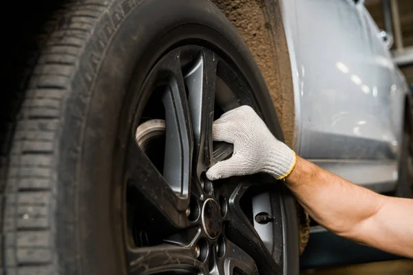 Cropped shot of repairman in protective glove examining car wheel at auto repair shop — Stock Photo