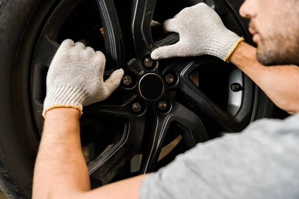 Partial view of auto mechanic in protective gloves checking automobile wheel at auto repair shop — Stock Photo