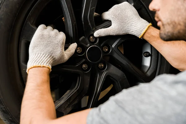 Vista parcial de mecánico automático en guantes de protección de control de rueda de automóvil en taller de reparación de automóviles - foto de stock