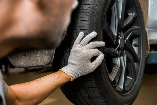 Cropped shot of repairman in protective glove examining car wheel at auto repair shop — Stock Photo