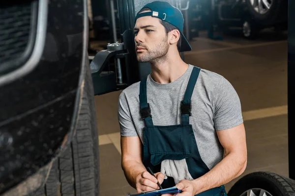 Young repairman with notepad checking car wheels at auto repair shop — Stock Photo