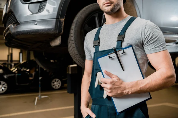 Vue partielle du réparateur avec bloc-notes à l'atelier de réparation automobile — Photo de stock