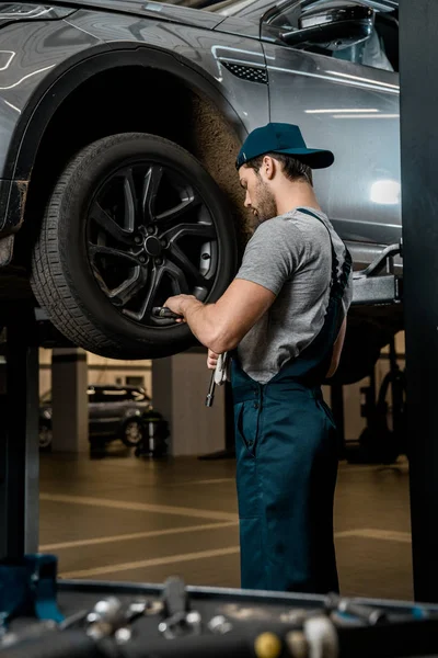 Auto mechanic in uniform fixing car wheel at auto repair shop — Stock Photo