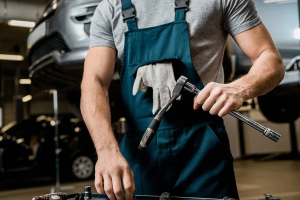 Partial view of auto mechanic in uniform with lug wrench at auto repair shop — Stock Photo