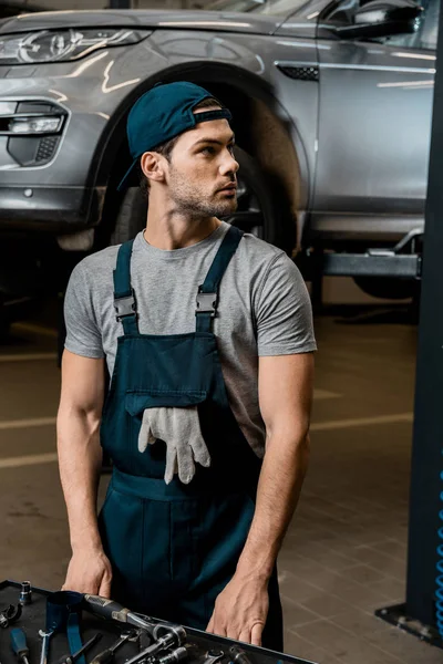 Junger Reparateur steht mit mechanischem Werkzeug an der Tischplatte in der Autowerkstatt — Stockfoto