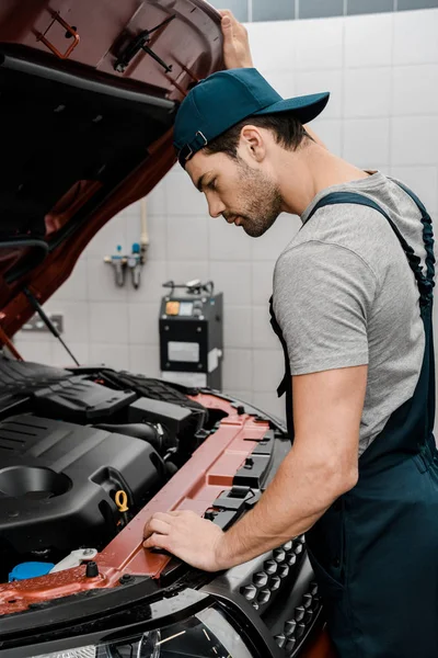 Vue latérale du réparateur examinant la voiture avec capot ouvert à l'atelier de réparation automobile — Photo de stock