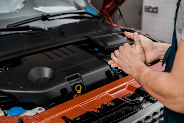 Cropped shot of repairman standing at car with opened cowl at auto repair shop — Stock Photo