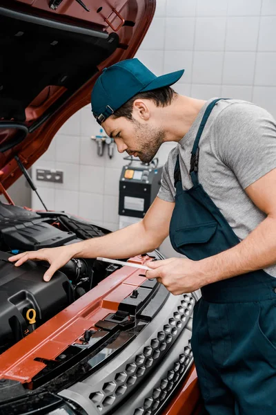 Side view of auto mechanic with tablet checking car cowl at mechanic shop — Stock Photo