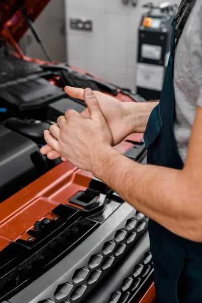 Cropped shot of repairman standing at car with opened cowl at auto repair shop — Stock Photo