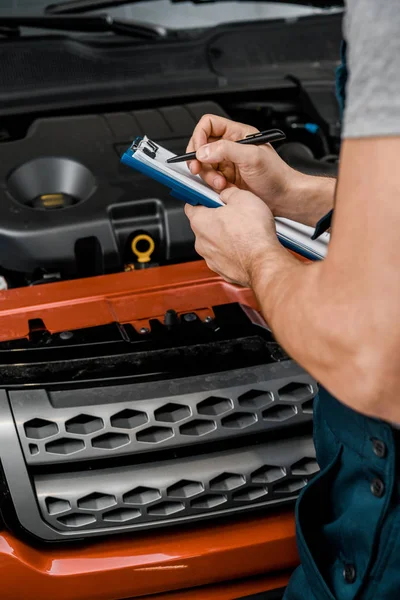 Partial view of repairman with notepad examining car at auto repair shop — Stock Photo