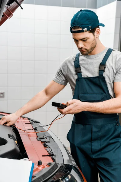 Young auto mechanic with multimeter voltmeter checking car battery voltage at mechanic shop — Stock Photo