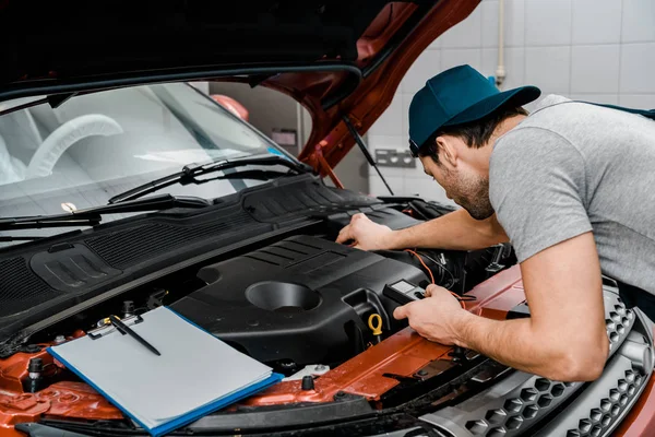 Automechaniker mit Multimeter-Voltmeter überprüfen Autobatteriespannung im Mechaniker-Geschäft — Stockfoto