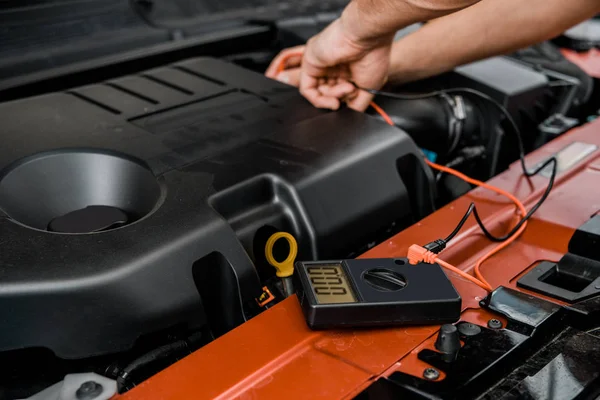 Vue partielle du mécanicien automatique avec voltmètre multimètre vérifiant la tension de la batterie de voiture à l'atelier de mécanique — Photo de stock