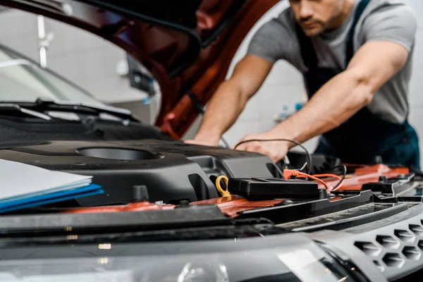 Cropped shot of auto mechanic with multimeter voltmeter checking car battery voltage at mechanic shop — Stock Photo