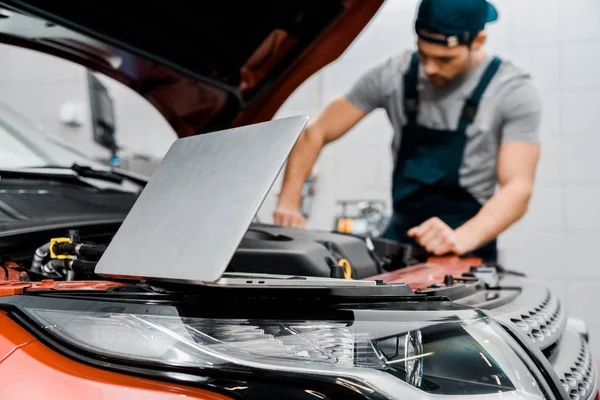 Selective focus of laptop and auto mechanic at auto repair shop — Stock Photo