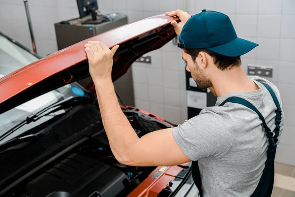 Vue latérale du mécanicien automobile examinant capot de voiture à l'atelier — Photo de stock