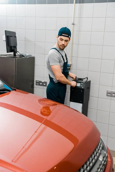 Young auto mechanic in uniform looking at new automobile at mechanic shop — Stock Photo