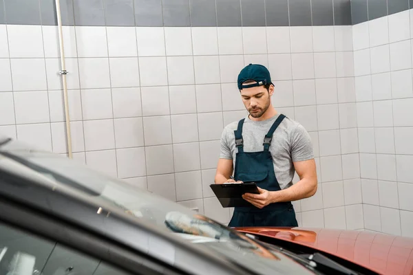 Portrait of auto mechanic with notepad examining car at auto repair shop — Stock Photo