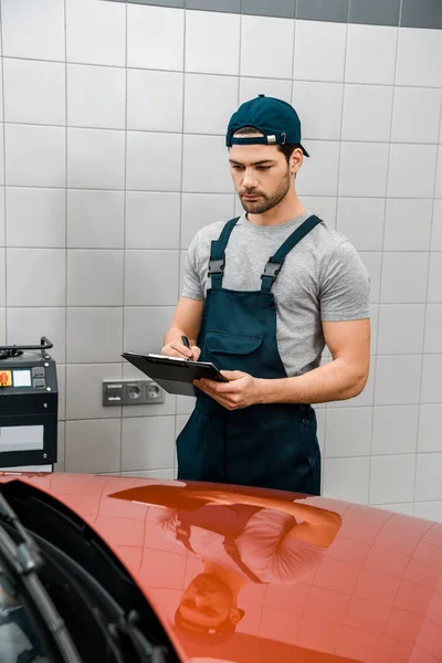 Focused auto mechanic with notepad examining new car at auto repair shop — Stock Photo