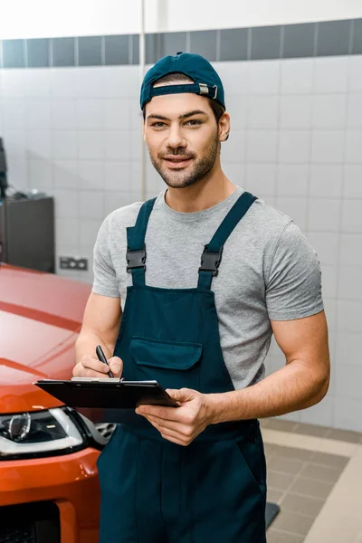 Portrait of auto mechanic with notepad looking at camera at auto repair shop — Stock Photo