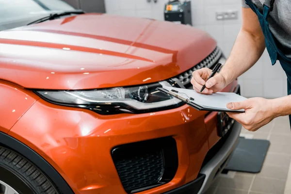 Vista parcial de mecánico auto con bloc de notas examinar coche nuevo en taller de reparación de automóviles - foto de stock