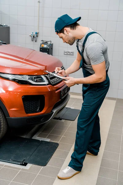 Auto mechanic with notepad examining car at auto repair shop — Stock Photo