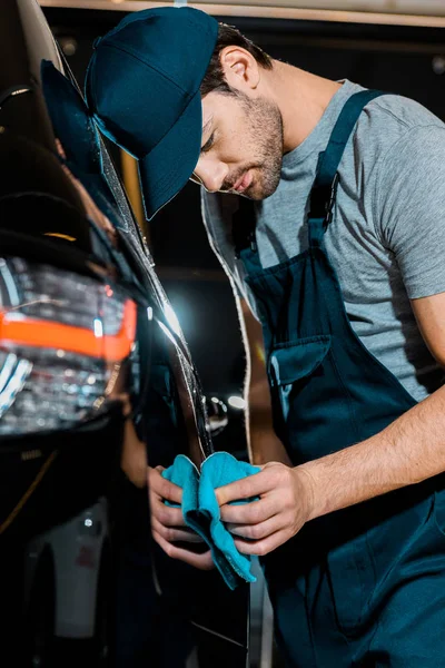 Young auto mechanic cleaning car with rag at auto repair shop — Stock Photo