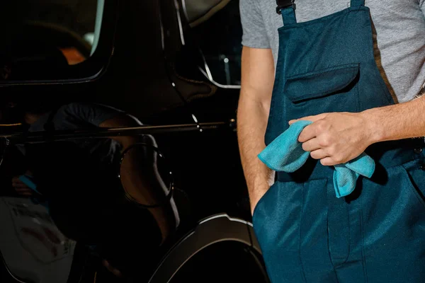 Vista parziale del meccanico con straccio in mano in piedi a macchina nera in officina di riparazione auto — Foto stock