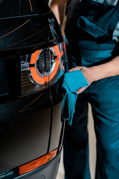 Partial view of auto mechanic cleaning black car with rag at mechanic shop — Stock Photo