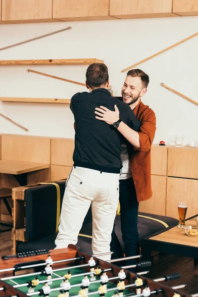 Веселі чоловіки обіймаються, вітаючи один одного в кафе — стокове фото