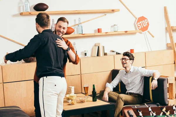 Smiling men hugging while greeting each other in cafe — Stock Photo